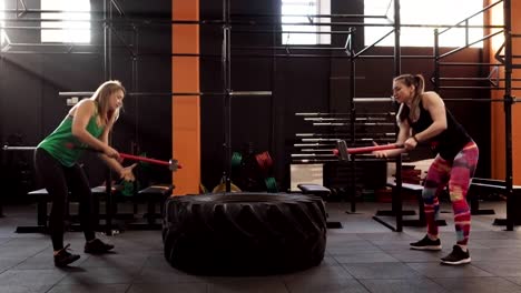 Team-of-two-fitness-women-doing-sledgehammer-swing-workout-together-in-gym