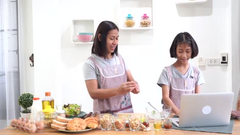 Mutter-und-Tochter-lernen-online-Kochen-mit-Laptop-Computer-in-der-Küche-zu-Hause
