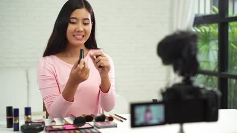 Blogger-de-belleza-actualmente-cosméticos-de-belleza-sentada-en-frente-la-cámara-para-la-grabación-de-vídeo.-Hermosa-mujer-use-cepillo-mientras-revisión-maquillaje-tutorial-transmiten-video-en-vivo-en-red-social-por-internet.