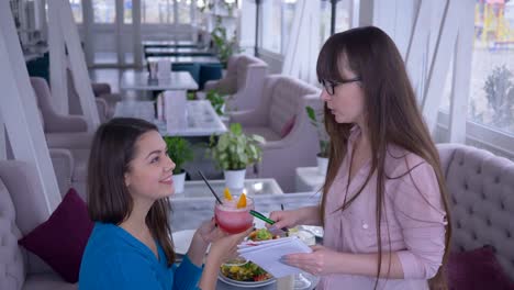 healthy-breakfast,-girl-with-notebook-and-pen-in-hand-writes-down-diet-plan-together-with-girlfriend-sitting-in-a-cafe