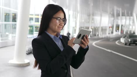 Señora-asiático-feliz-comunicarse-por-mensajería-en-tableta-en-aeropuerto