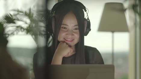 Young-Asian-woman-typing-on-laptop-while-listening-to-music-over-headphones