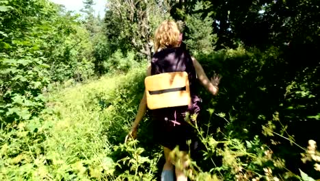 Touristen-Frau-mit-einem-Rucksack-zu-Fuß-in-ein-Feld-von-Wildblumen-in-einem-Nationalpark-in-den-Wald-im-Sommer.-Mädchen-berührt-den-Rasen