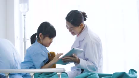 Female-doctor-showing-digital-tablet-computer-and-talking-with-young-patient-girl-with-happy-emotion.