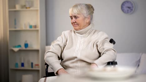 Sad-old-woman-in-wheelchair-looking-at-untasty-dinner-in-medical-center,-sorrow