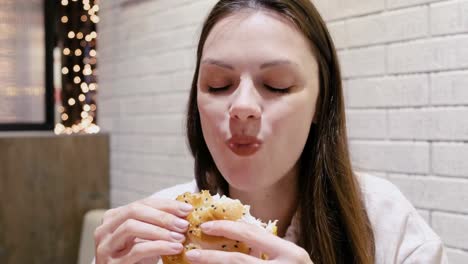 Woman-eating-a-hamburger-with-relish-and-delight-in-cafe.