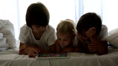 Brothers,-playing-in-bed-on-tablet,-enjoying-their-summer-holiday