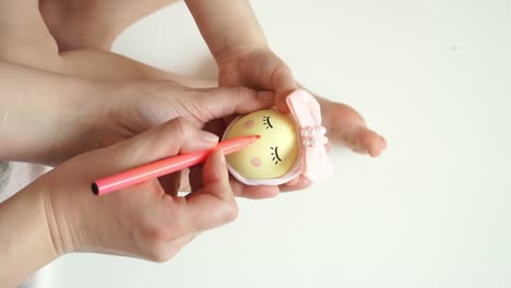 Women's-and-children's-hands-hold-chicken-egg-decorated-for-Easter-chick,-draw-chicken-muzzle-with-marker.