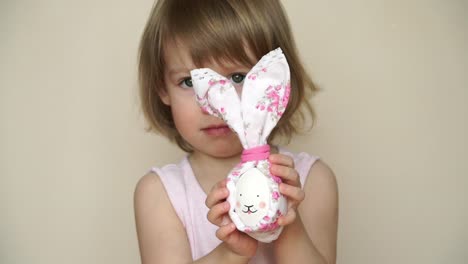 Portrait-of-little-cute-child-girl-laughs-and-smiles-holding-in-hand-chicken-egg-decorated-for-Easter-bunny.