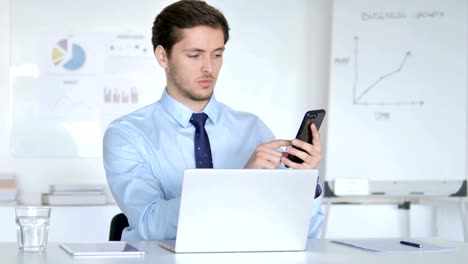 Young-Businessman-Using-Smartphone-and-Laptop-for-Work