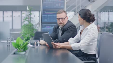 En-la-sala-de-reuniones-ejecutivo-femenino-muestra-tableta-digital-de-ordenador-a-inversor-masculino,-que-discutir-estadísticas-y-el-potencial-de-inversión-de-empresas.-Oficina-Corporativa-ocupada-con-empresarios-que-trabajan