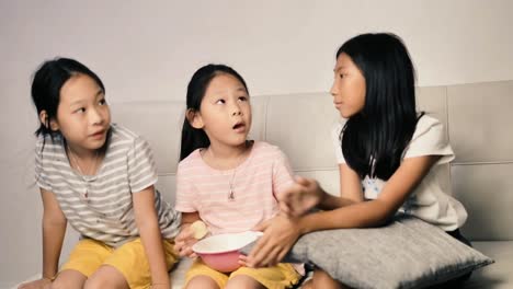 Glückliches-asiatisches-Mädchen-essen-Chips-mit-der-Familie-und-sprechen-zusammen-zu-Hause-in-der-Nacht.