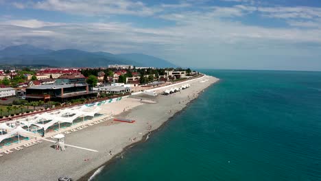 Toma-de-video-aéreo.-La-costa-del-mar-negro-de-Sochi,-Rusia.-Vistas-a-la-montaña.-Un-lugar-de-descanso-y-entretenimiento.-Hoteles-y-casas-en-la-costa.-Infraestructura-para-recreación-y-entretenimiento.