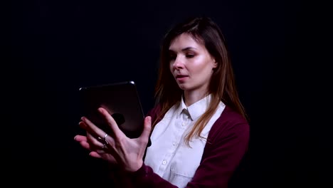 Portrait-of-young-brunette-businesswoman-making-beautiful-selfie-photos-on-tablet-happily-on-black-background.