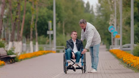 Young-man-gets-up-from-the-wheelchair-and-walks-over.-Father-helps-his-son-get-up-from-the-wheelchair-and-walk.