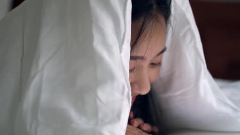 Close-up-portrait-Asian-woman-smiling-and-using-a-tablet-on-the-bedroom-browsing-online-social-media-sharing-lifestyle.