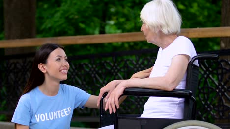 Volunteer-talking-with-handicapped-old-lady-in-wheelchair-at-nursing-home-park