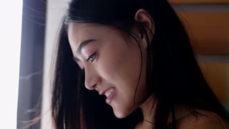 Close-up-a-smiling-portrait-of-a-beautiful-caucasian-Asian-woman-using-smartphone-shopping-online-and-use-the-credit-card-payment-while-standing-beside-the-window-at-the-office-room.