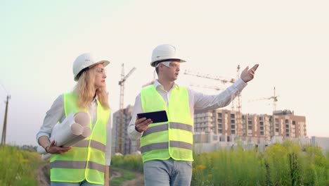 Ingenieur-und-Controller-gehen-auf-die-Baustelle-vor-dem-Hintergrund-von-Kränen-und-sprechen-über-Die-Arbeit.-Diskussion-mit-dem-Bauunternehmer-über-den-Baufortschritt