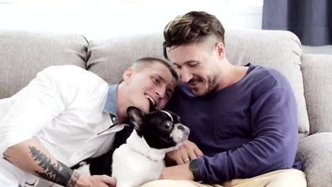 Pareja-gay-relajándose-en-el-sofá-con-perro.-Disfruta-alimentando-a-un-perro-por-la-boca.