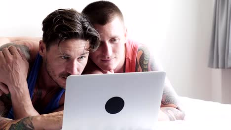 Gay-couple-in-bed-using-laptop-computer.-Using-keyboard.