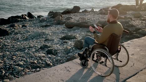 Disabled-man-surfing-net-on-mobile-while-relaxing-by-the-sea