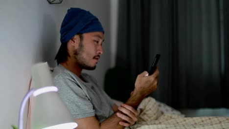 Attractive-Asian-man-using-a-mobile-phone-while-Lying-on-Bed-at-home.-Searching-social-media-and-watching-a-video.