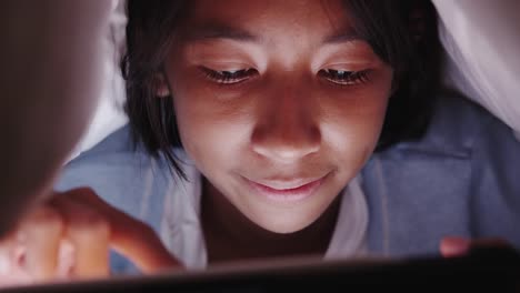 Nahaufnahme-von-asiatischen-kleinen-Mädchen-mit-Tablet-unter-Decke-im-Schlafzimmer-in-der-Nacht