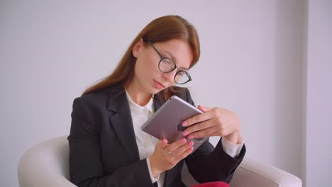 Retrato-de-primer-plano-de-joven-empresaria-caucásica-en-gafas-escribiendo-en-la-tableta-mirando-ta-cámara-sonriendo-felizmente-sentado-en-el-sillón