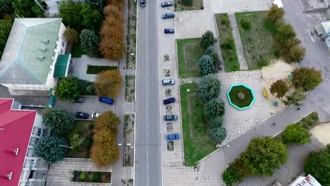 Impresionante-vista-de-pájaro-de-una-carretera-recta-con-coches-en-movimiento-pasando-por-una-ciudad-verde-con-edificios-agradables-y-árboles-bien-cuidados-en-verano