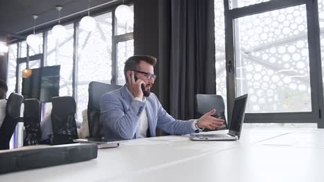 Serio-hombre-de-negocios-altamente-calificado-discutiendo-proyecto-de-computadora-por-teléfono-con-interlocutor-sentado-en-el-lugar-de-trabajo-de-la-oficina