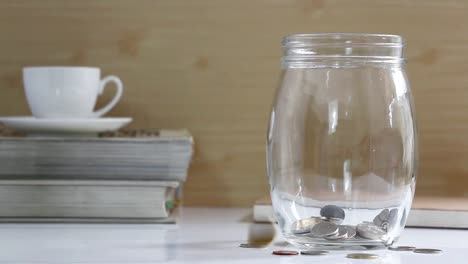 Coins-in-a-glass-jar-on-the-table.-Coins-falling-into-a-jar.