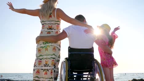 husband-in-wheel-chair-hug-wife-and-little-girl-in-backlight,-disabled-hugs-his-wife-and-daughter,-invalid-with-pregnant