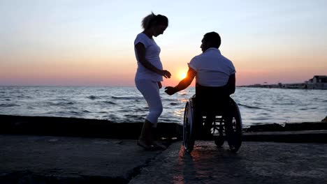 Discapacitados-y-la-mujer-Levante-las-manos-en-la-noche,-minusválidos-con-puesta-de-sol-viendo-niña-embarazada,-esperando-bebé,-marido