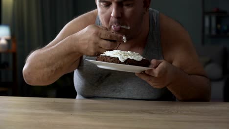 Hombre-adulto-con-sobrepeso-engullendo-tarta-y-lamiendo-sus-dedos,-diabetes,-comida-chatarra