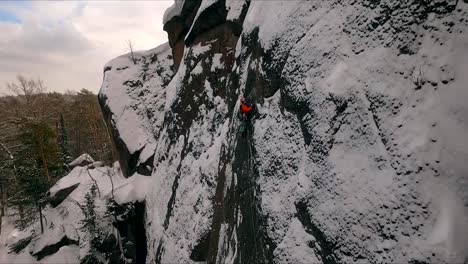 Aerial-view-of-a-rock-climber-climbing-a-steep-cliffs-during-a-sunny-winter-day.