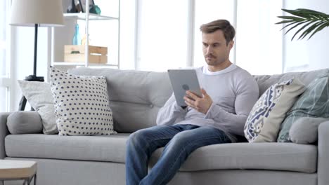 Ernster-Mann-mit-Tablet-sitzend-auf-Sofa