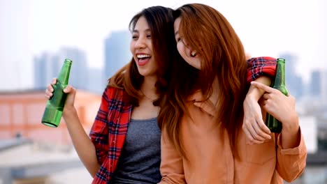 Slow-motion-young-asian-woman-lesbian-couple-clinking-bottles-of-beer-party-on-rooftop.