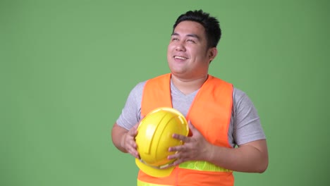 Young-handsome-overweight-Asian-man-construction-worker-against-green-background