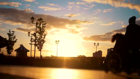 Hombre-con-un-niño-caminando-en-el-muelle-pasado-lleva-hombre-joven-en-silla-de-ruedas-al-atardecer