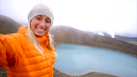 Slow-Motion-junge-Frau-mit-orange-Regenmantel-unter-Selfie-Porträt-mit-Vulkanlandschaft-in-Island.-Die-Leute-reisen-Exploration-Konzept