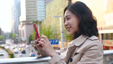 Bastante-feliz-joven-mujer-asiática-mediante-teléfono-móvil-en-la-ciudad-China-de-Chengdu,-en-la-tarde-en-el-puente-con-la-carretera-muy-transitada-en-el-fondo