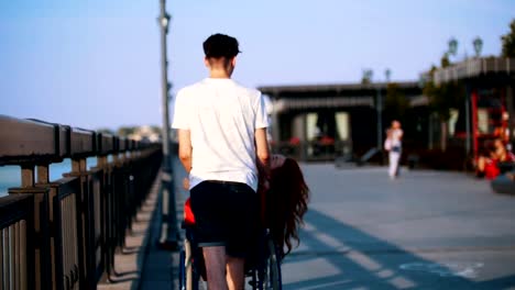 Guy-rollt-ein-behindertes-Mädchen-mit-den-roten-Haaren-In-einem-Rollstuhl-direkt-am-Wasser