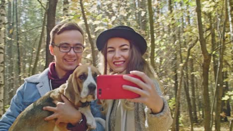 Fröhliches-paar-mit-einem-Hund-nehmen-Foto-im-Herbst-park