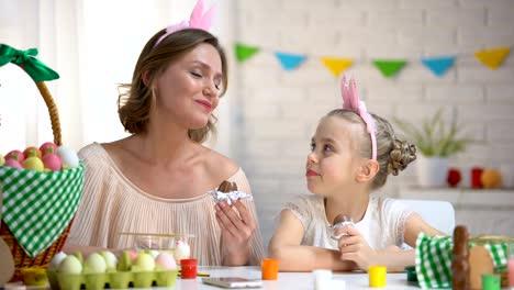 Schöne-Mutter-und-Tochter-in-lustige-Stirnbänder-essen-Schokolade-Ostereier