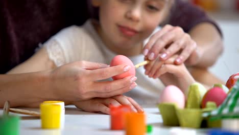 Mother-teaching-daughter-to-paint-Easter-eggs-brush,-family-holiday-traditions