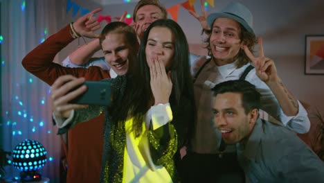 Glückliche-Gruppe-von-jungen-Leuten-unter-kollektiven-Selfie-auf-wilde-Hausparty.-Neon-Licht,-Disco-Kugel-und-lustige-Kostüme.