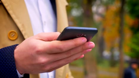 Primer-plano-de-mano-masculina-sosteniendo-smartphone-moderno-y-gestión-en-el-fondo-de-aire-libre-de-la-naturaleza