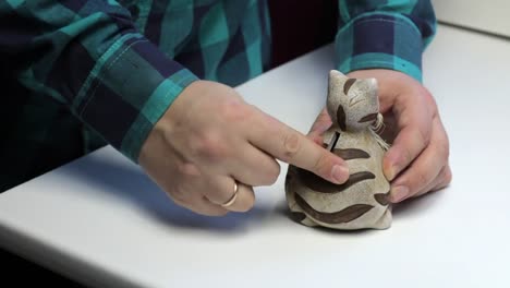 On-the-table-is-a-piggy-bank-in-the-form-of-a-cat.-A-man-holds-coins-in-his-hand-and-puts-them-in-a-piggy-bank.