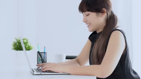 Hermosa-joven-freelance-mujer-asiática-sonriendo-trabajando-y-escribiendo-en-la-computadora-portátil-en-la-oficina-de-escritorio-con-profesional,-chica-usando-Notebook-comprobando-correo-electrónico-o-red-social,-negocio-y-concepto-de-estilo-de-vida.